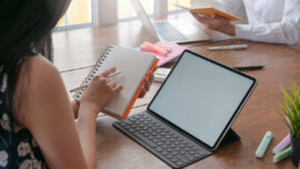 A woman with a notebook and a pen in her hand with a laptop on t
