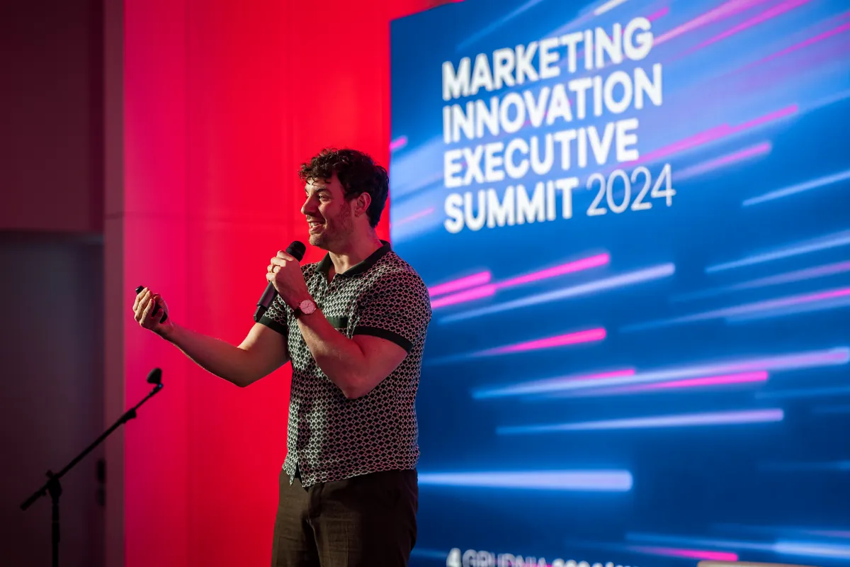 Uśmiechnięty prelegent z mikrofonem na scenie konferencji Marketing Innovation Executive Summit 2024